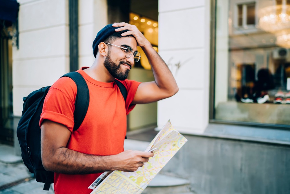 A man in a street holding a map confused on the direction he should take.