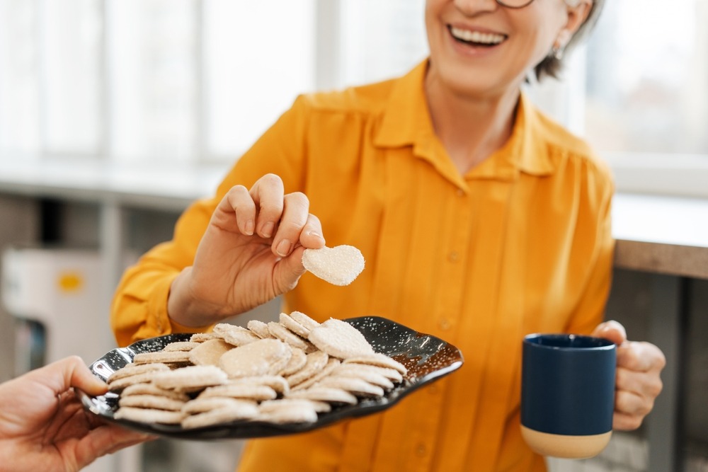A woman smiling taking a cookie held out to her.
