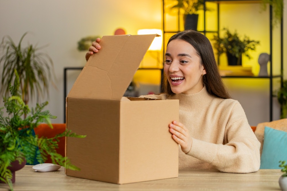 A woman opening an unlabelled box with a big smile on her face showing the real impact of customer satisfaction. 