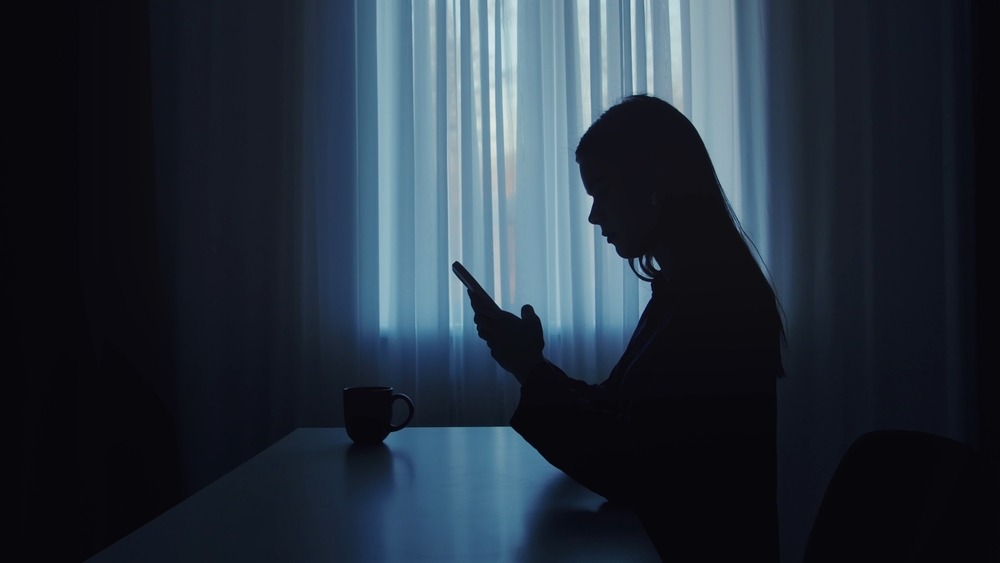 A silhouette of a woman sitting at a table using her phone, indicating the difficulties of tracking dark social marketing.