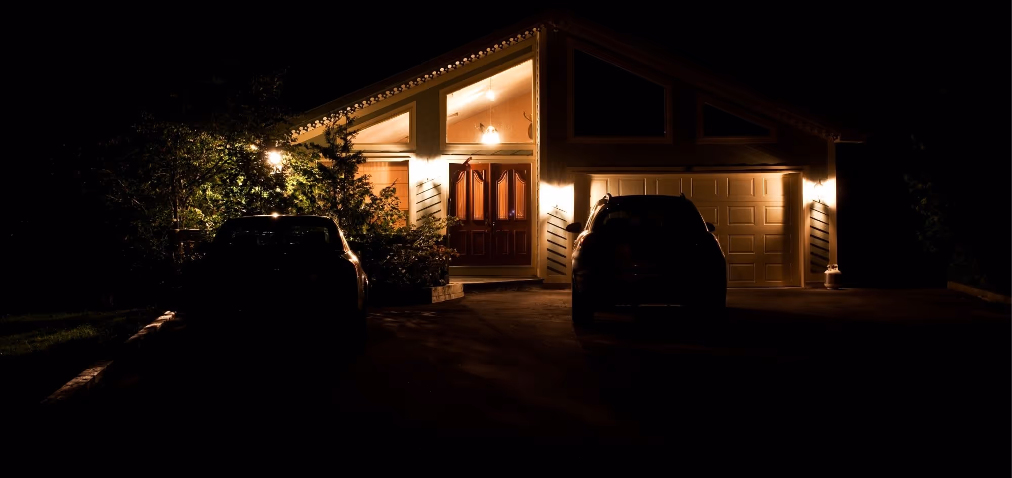 Ein modernes Haus bei Nacht mit Aussenbeleuchtung und geparkten Autos davor.