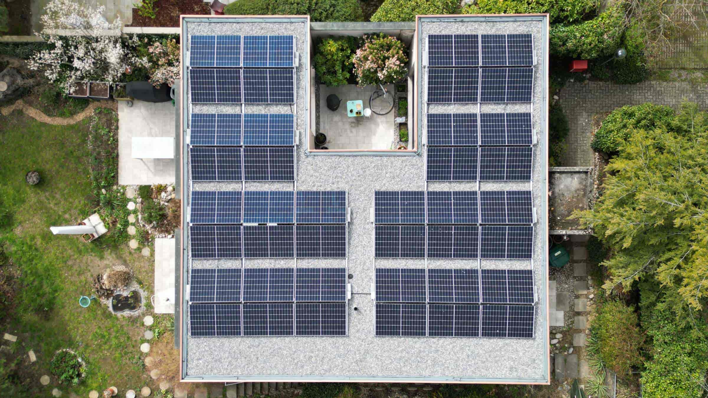Luftaufnahme eines Einfamilienhauses mit bekiestem Flachdach und einer Aufdach Solaranlage im Grünen.