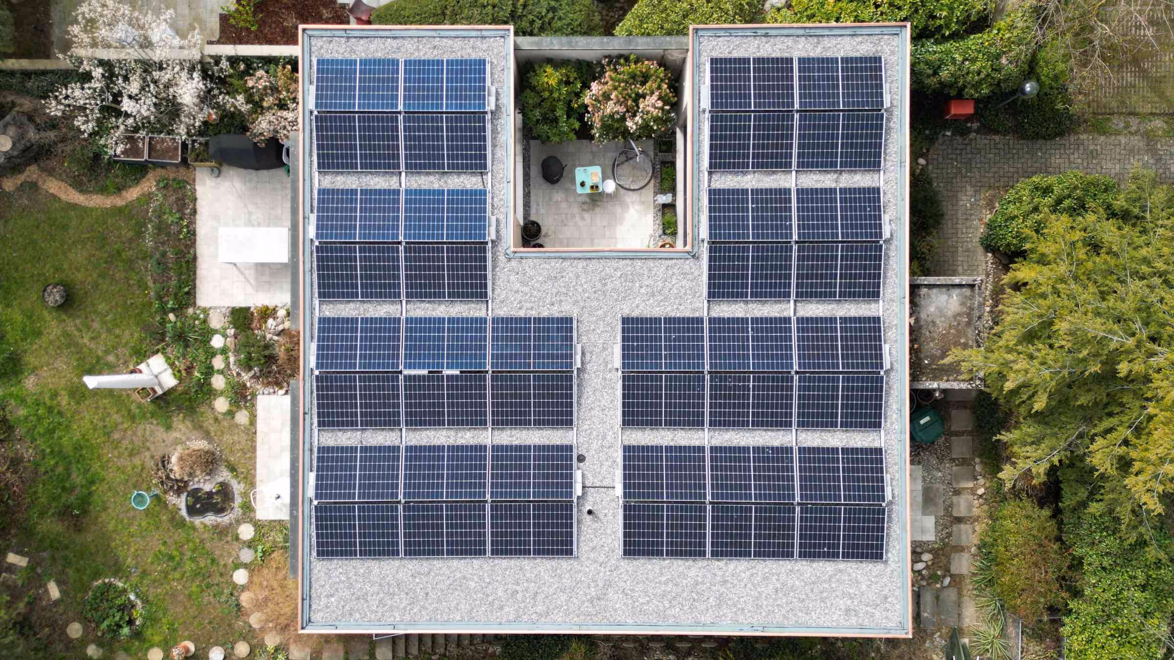Luftaufnahme eines Einfamilienhauses mit bekiestem Flachdach und einer Aufdach Solaranlage im Grünen.