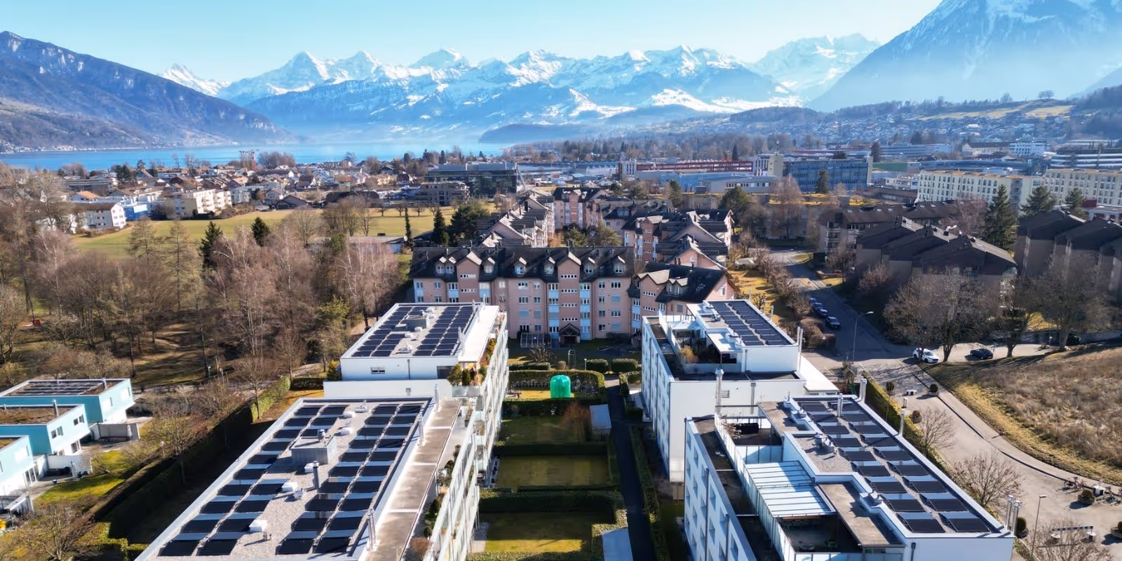 Luftansicht von vier Mehrfamilienhäuser mit Solaranlagen im Hintergrund Wohnquartiere in Thun, Thunersee und Berpanorama