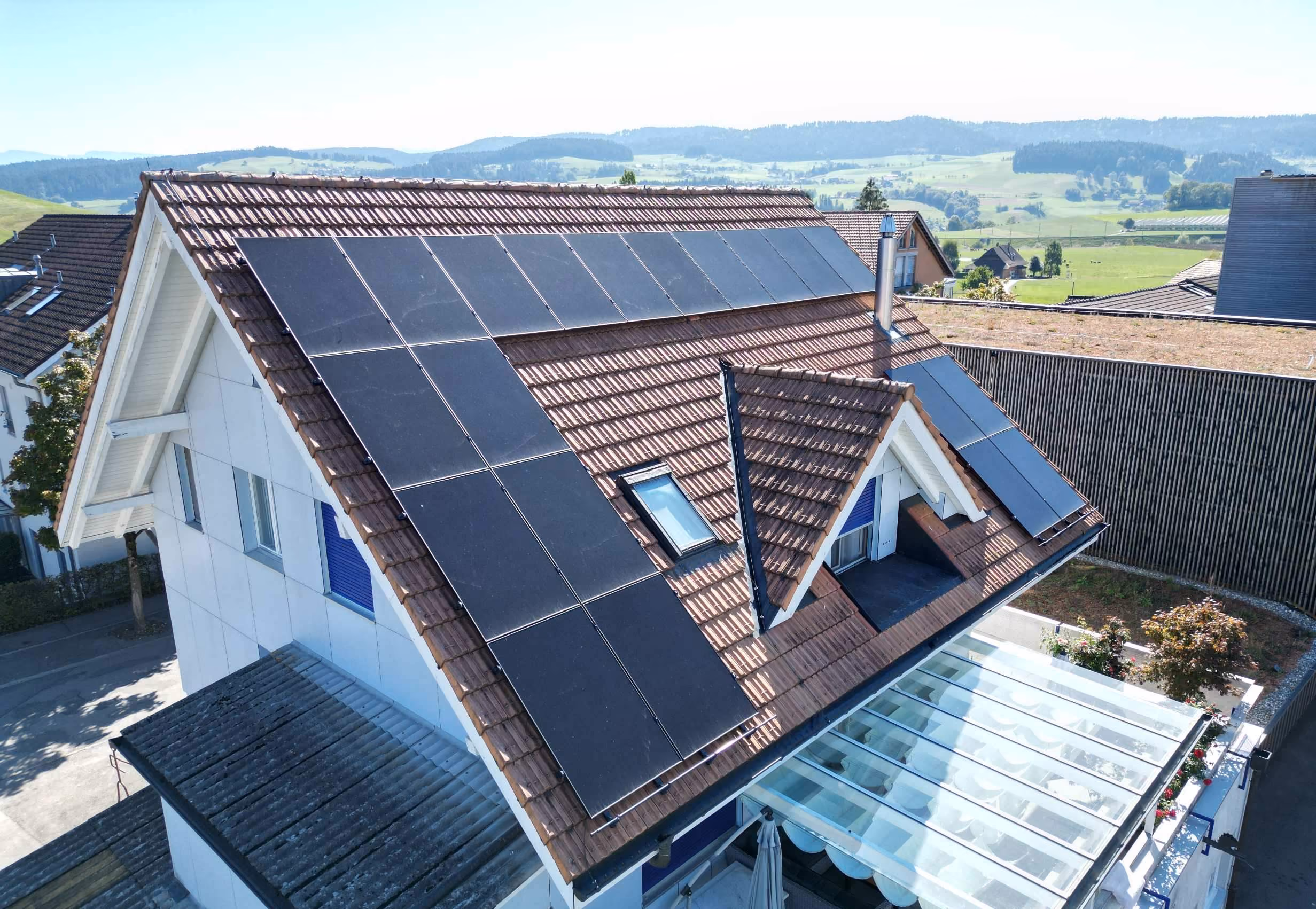 Landschaftsfoto aus Luftperspektive, zeigt vier Mehrfamilienhäuser mit Solaranlagen auf den Flachdächern, im Hintergrund Thunersee und Bergpanorama.
