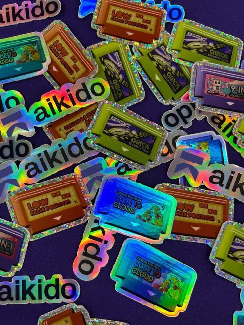 Holographic stickers on a dark surface with words like 'aikido,' 'LOW FALSE POSITIVES,' 'QUICK SECURITY FIXES,' and 'COVERS YOU FROM CODE TO CLOUD.'
