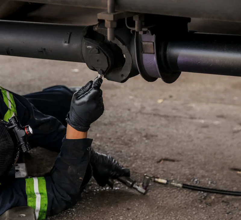 Driveline repair on a heavy-duty truck with technician lubricating driveline and universal joint components during service.