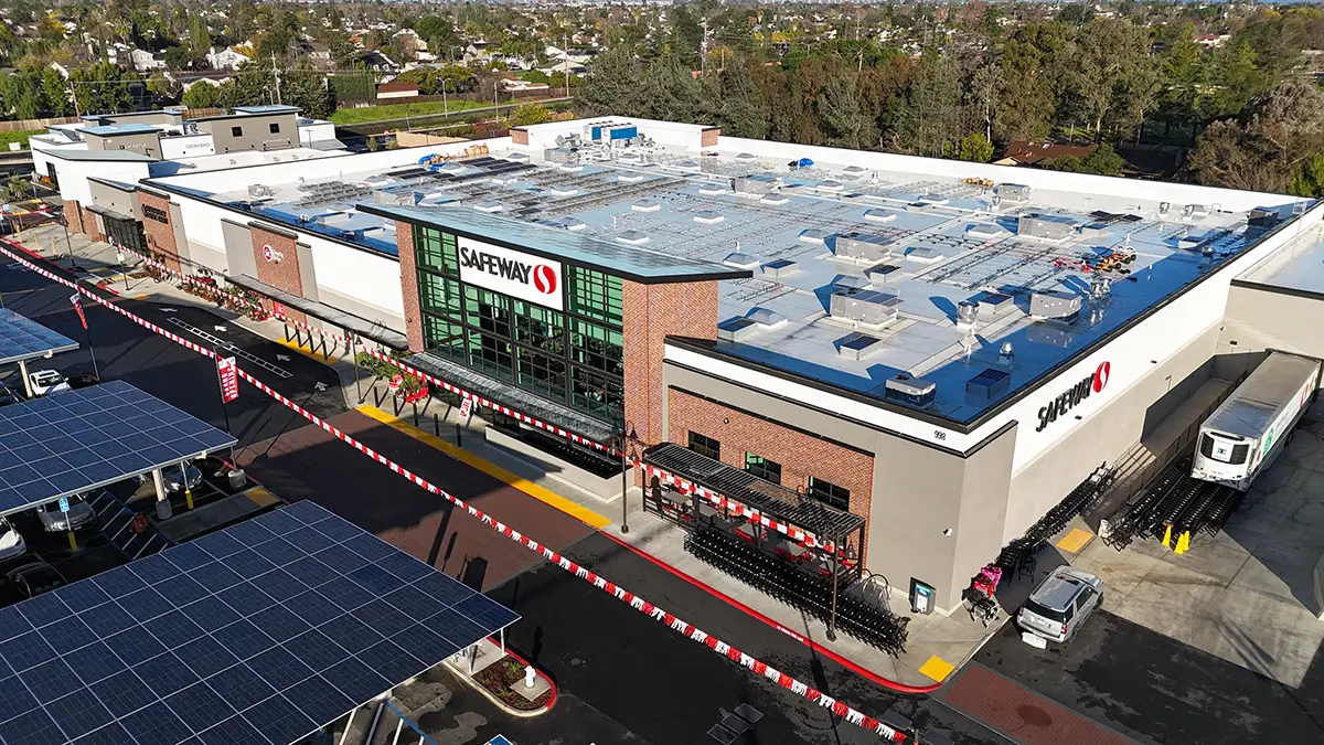 Aerial view of a large Safeway supermarket with solar panel-covered parking lot and shopping carts lined up outside.