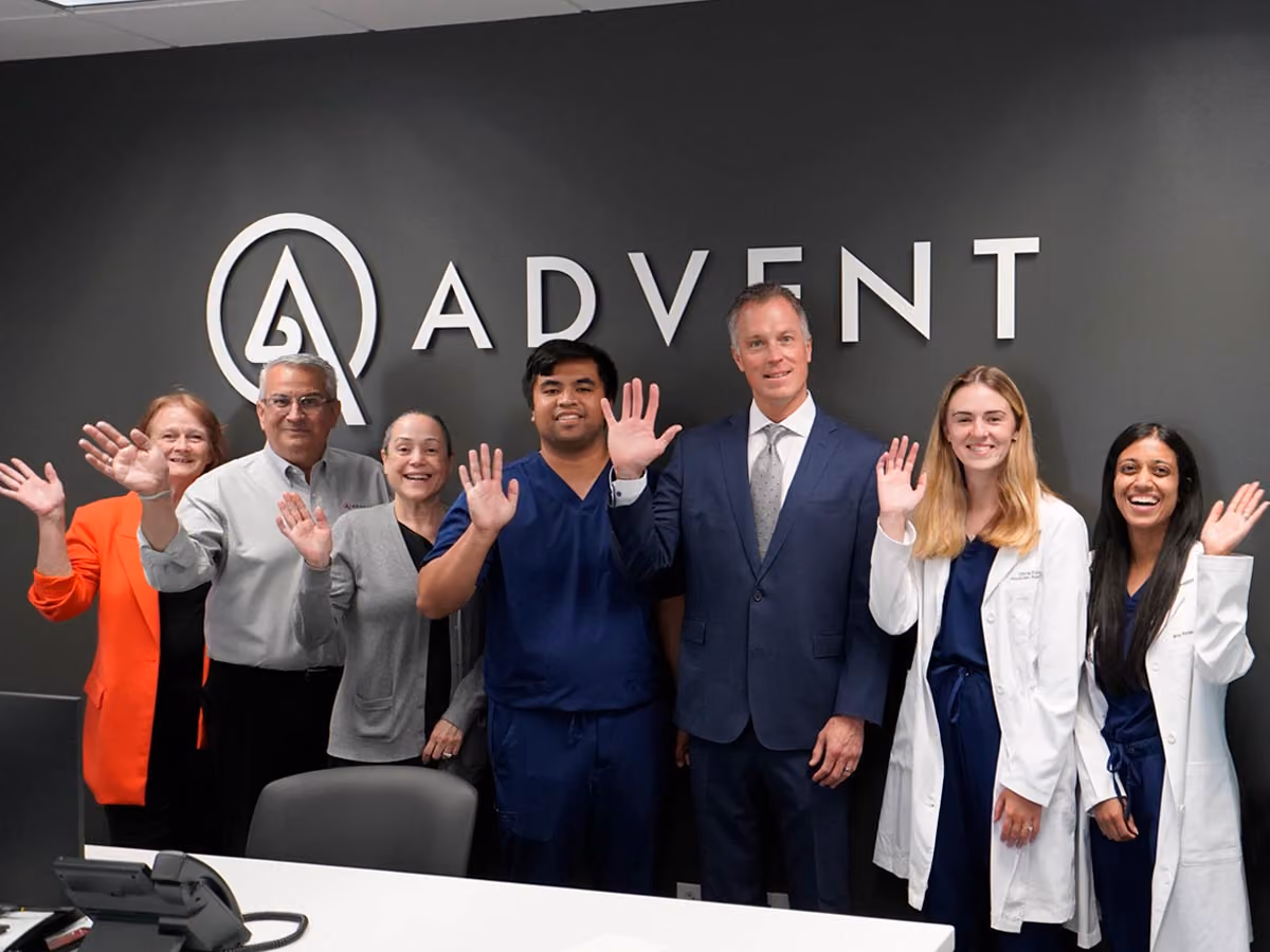 ADVENT Schaumburg Employees Standing in Front of the ADVENT Logo Smiling and Waving - 1200x900