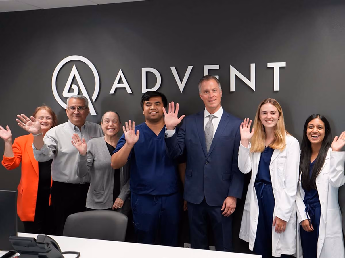 ADVENT Schaumburg Employees Standing in Front of the ADVENT Logo Smiling and Waving
