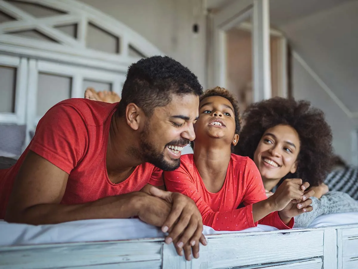 Family in Bed in Red Shirts Smiling and Laughing After a Great Nights Sleep - 1200x900