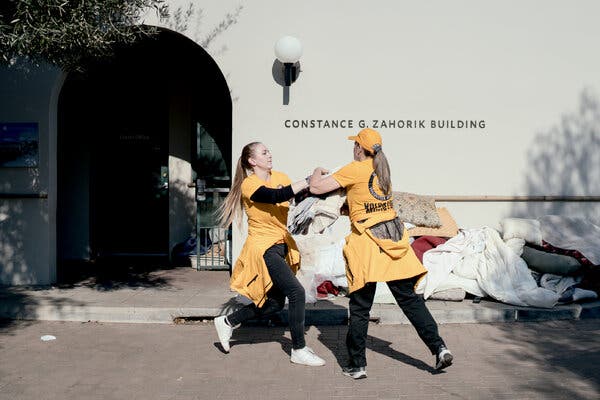 Two women wearing yellow and black carry blankets.