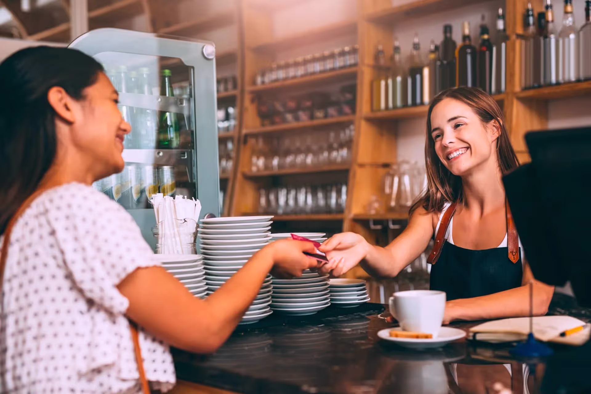 Una cliente pagando con su tarjeta de crédito mientras se sonríen con la chica que atiende la cafetería