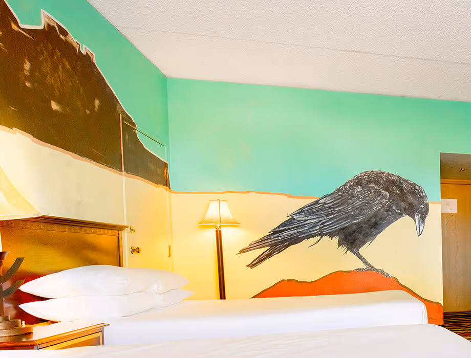 Colorful Artist guestroom with mural on the wall with a crow with king bed with white bedding