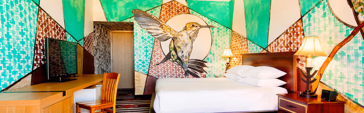Colorful Artist guestroom with mural on the wall with hummingbird and king bed with white bedding