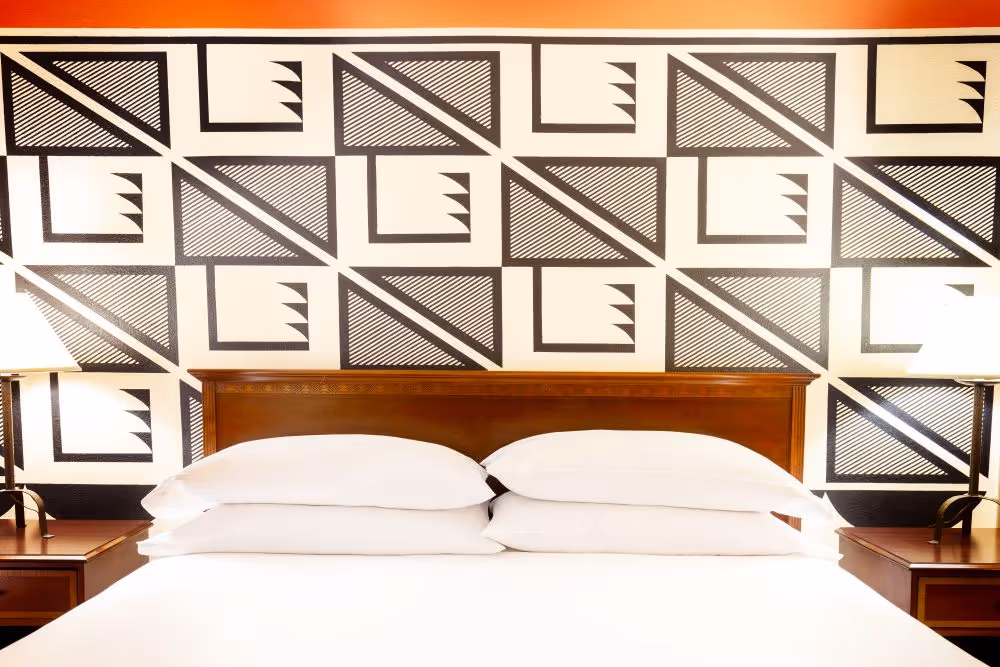 Artist guestroom with geometric patterned mural on the wall with king bed with white bedding