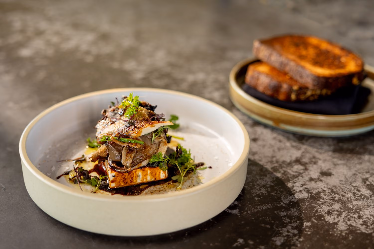 Dish with stacked mushroom and feta dish with a plate with bread in background