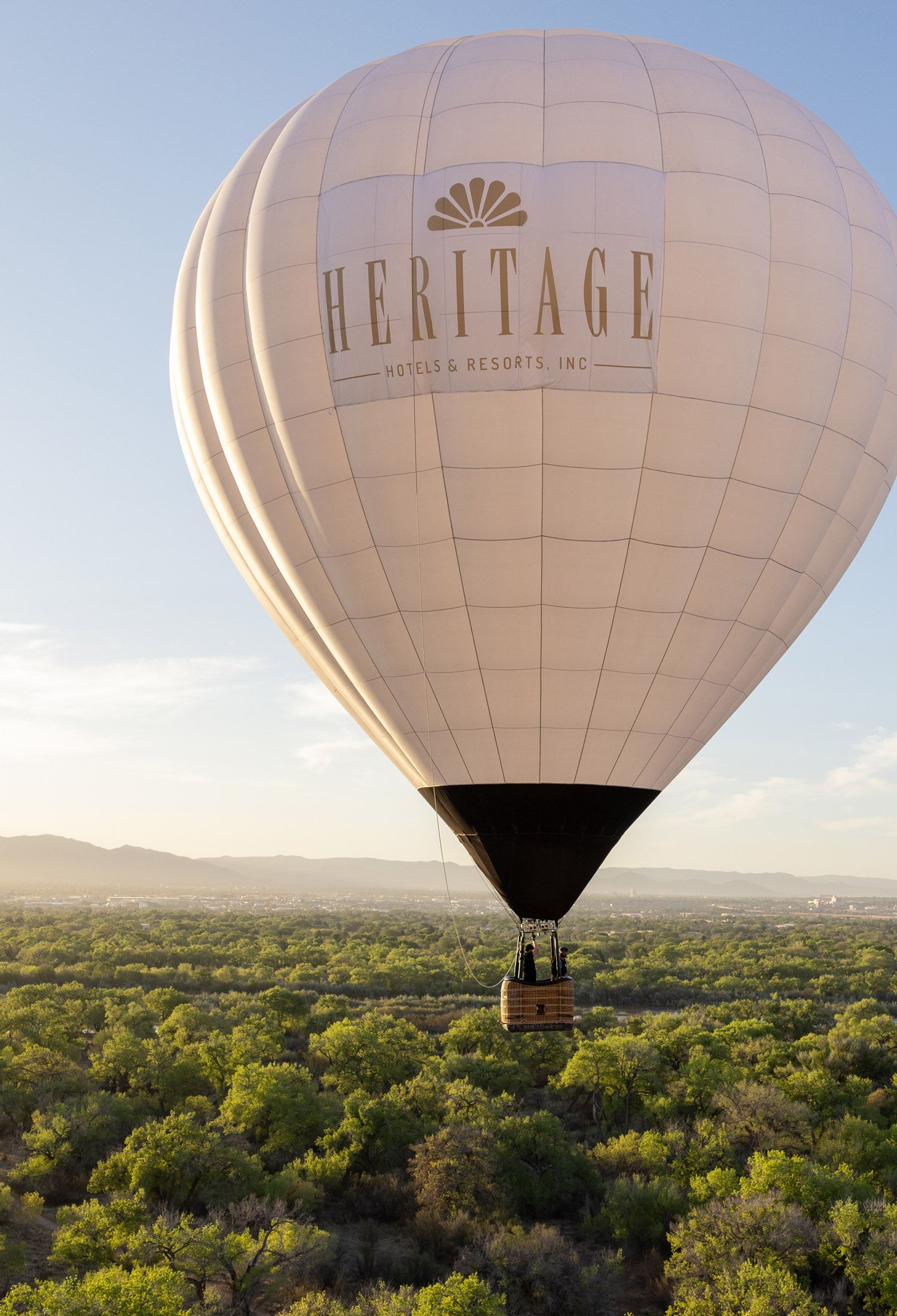 White hot air balloon with Heritage Hotels & Resorts logo in flight above Rio Grande and Bosque