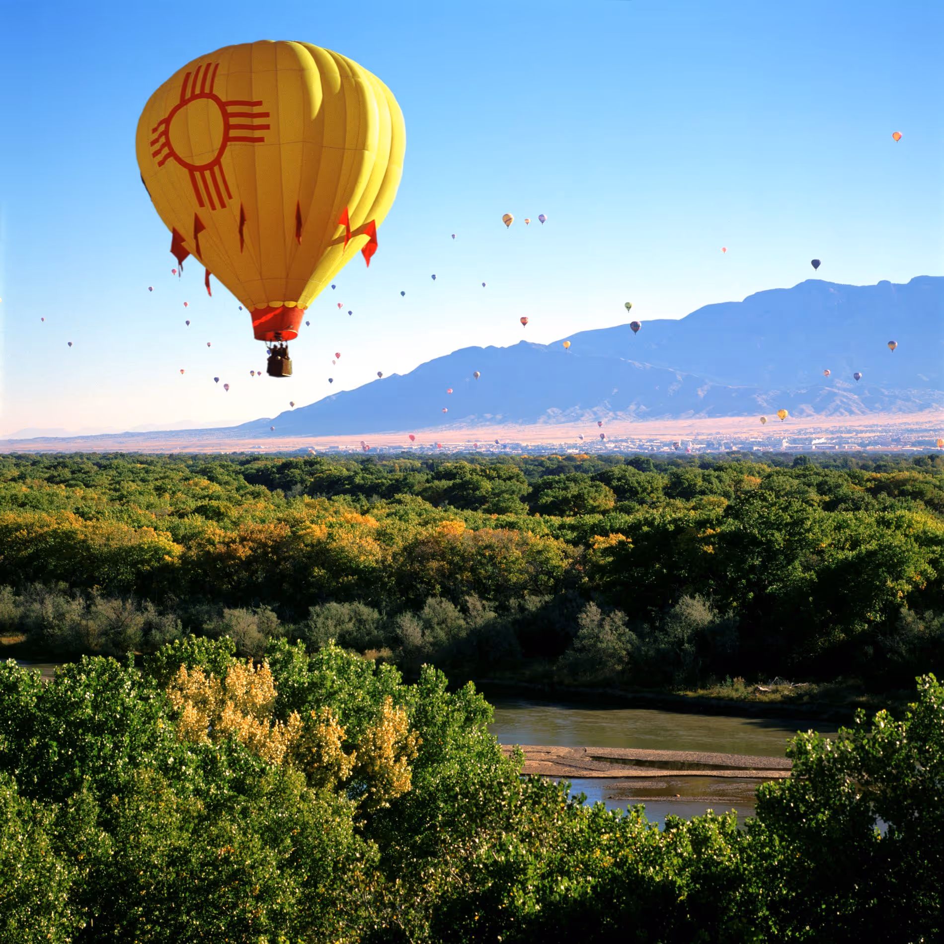 Yellow hot air balloon in flight over Rio Grande during Balloon Fiesta with a Zia symbol