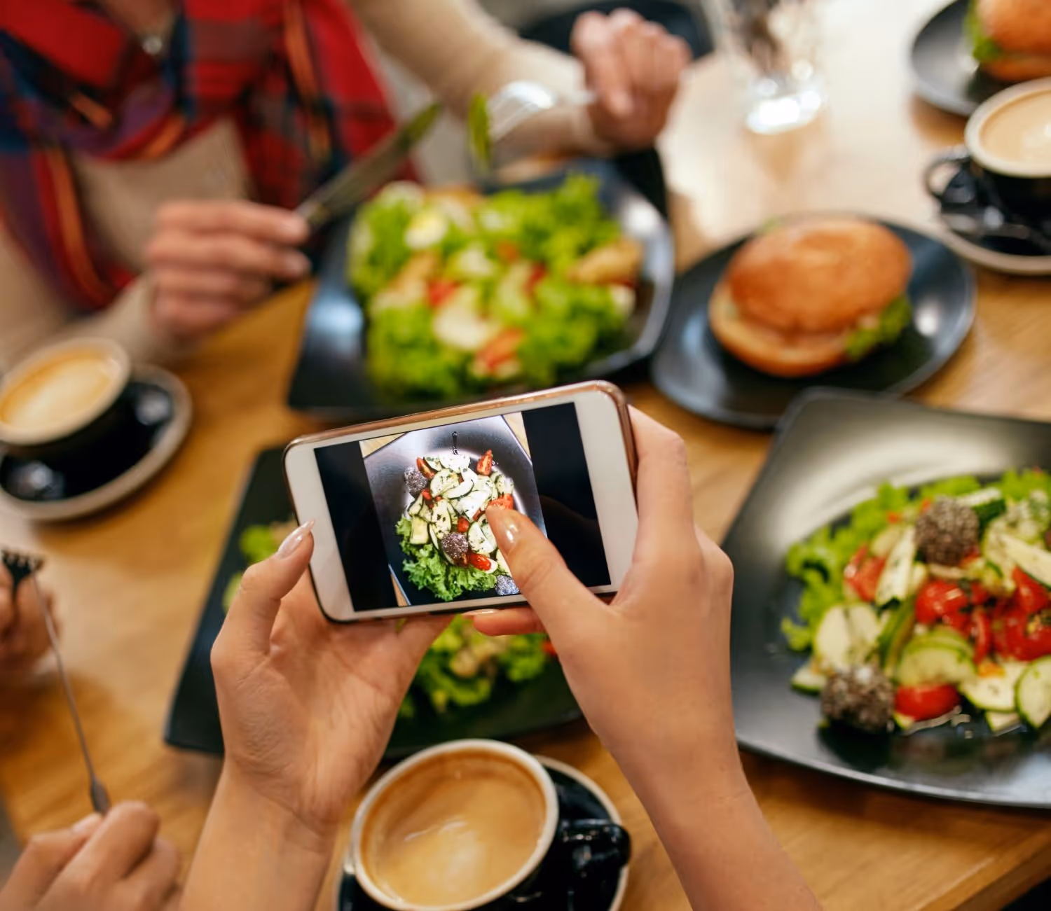 Person photographing their plates on a table of salads and drinks