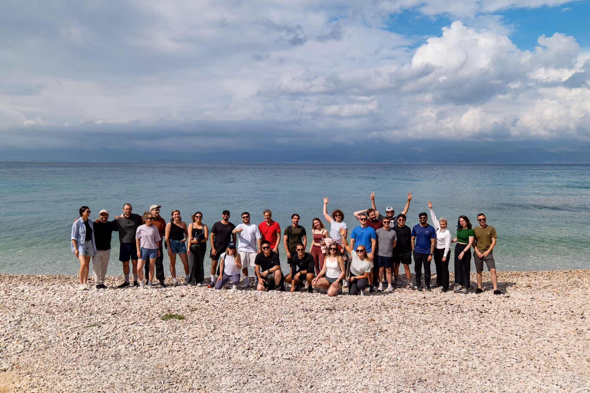 Group of people posing on a rocky beach with calm ocean and cloudy sky in the background.