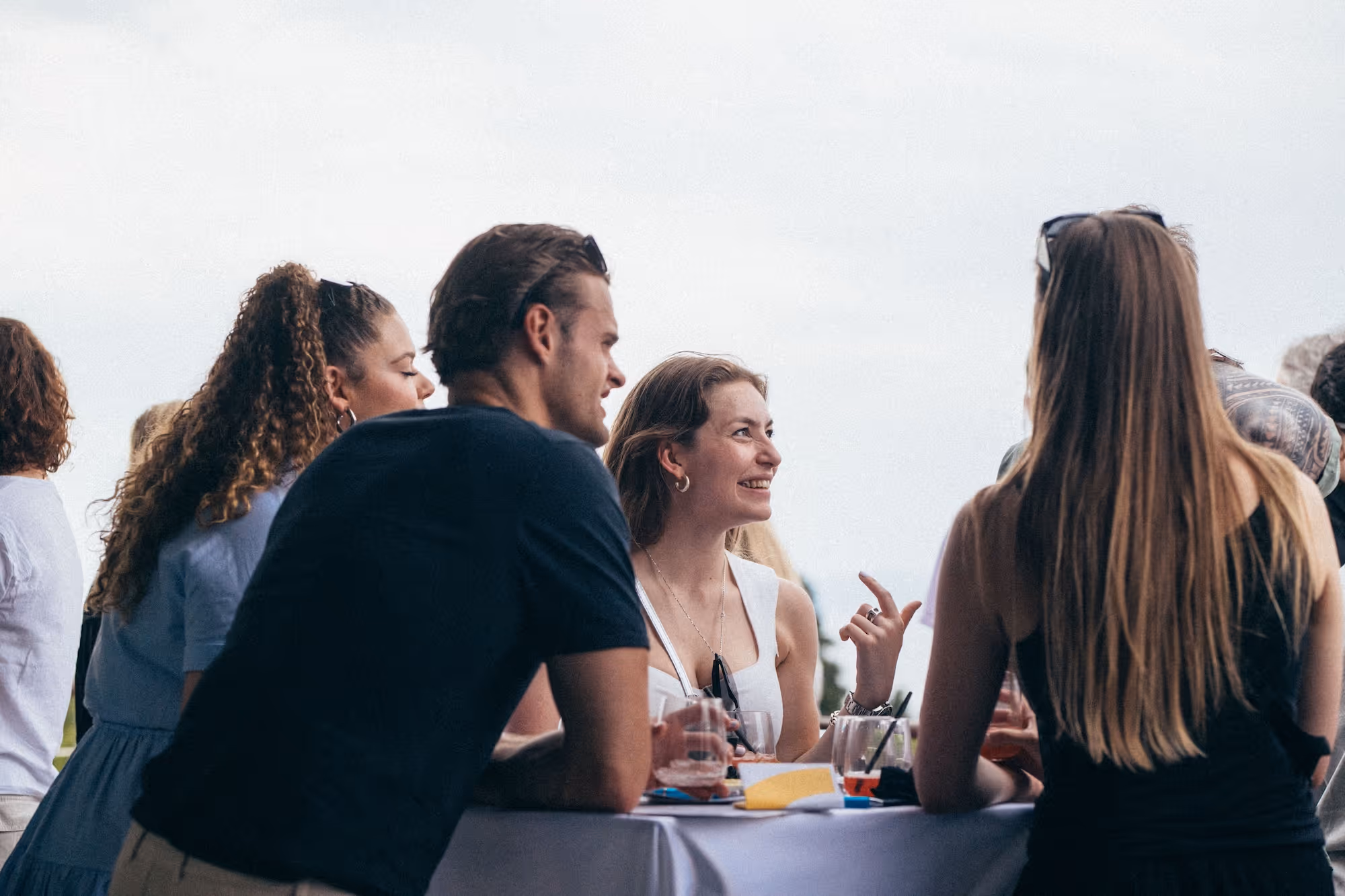 Group of young adults socializing and smiling around a table at an outdoor event.