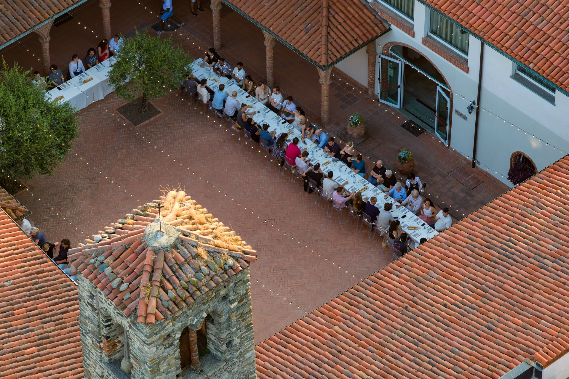 A long communal dinner in a Tuscan cloister courtyard at dusk