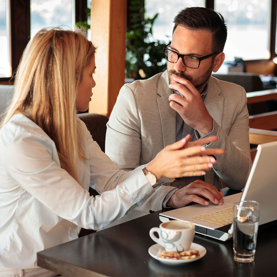 Stockbild: Zwei Arbeitskollegen sitzen im Café am Laptop und unterhalten sich.