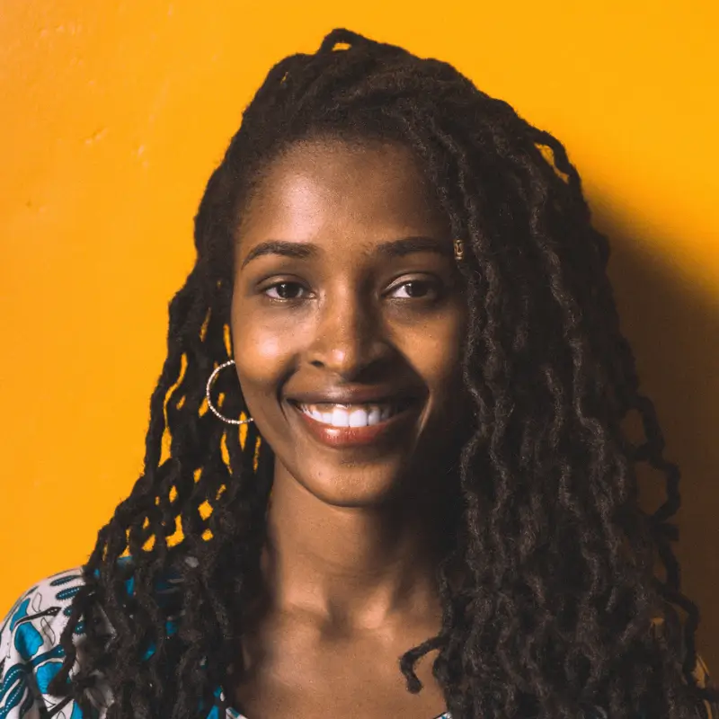 Gloria Mugabekazi, a black woman with braided hair, smilling in front of a yellow background.