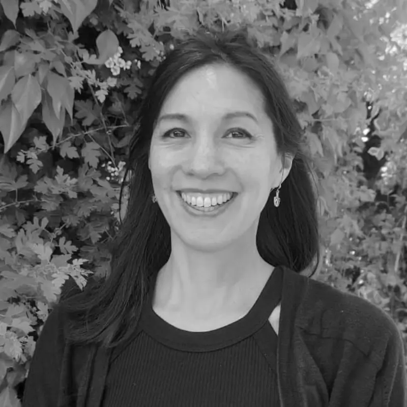 A black and white profile picture of Julia Minnear, a person with long straight hair smiling in front of greenery