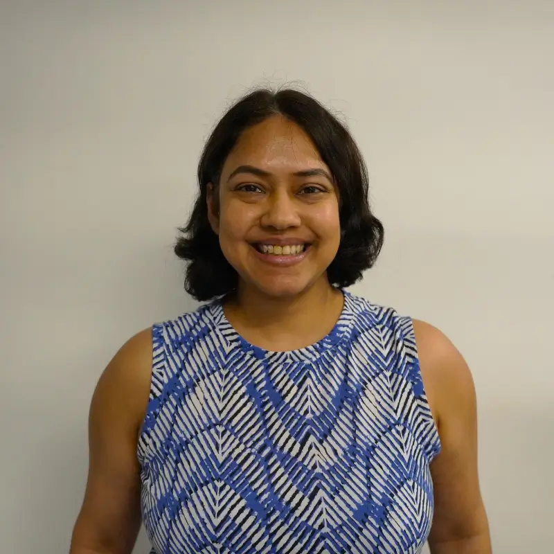 Payal Biswas, a person with black short hair wearing a white and blue patterned shirt and smiling in front of a white background