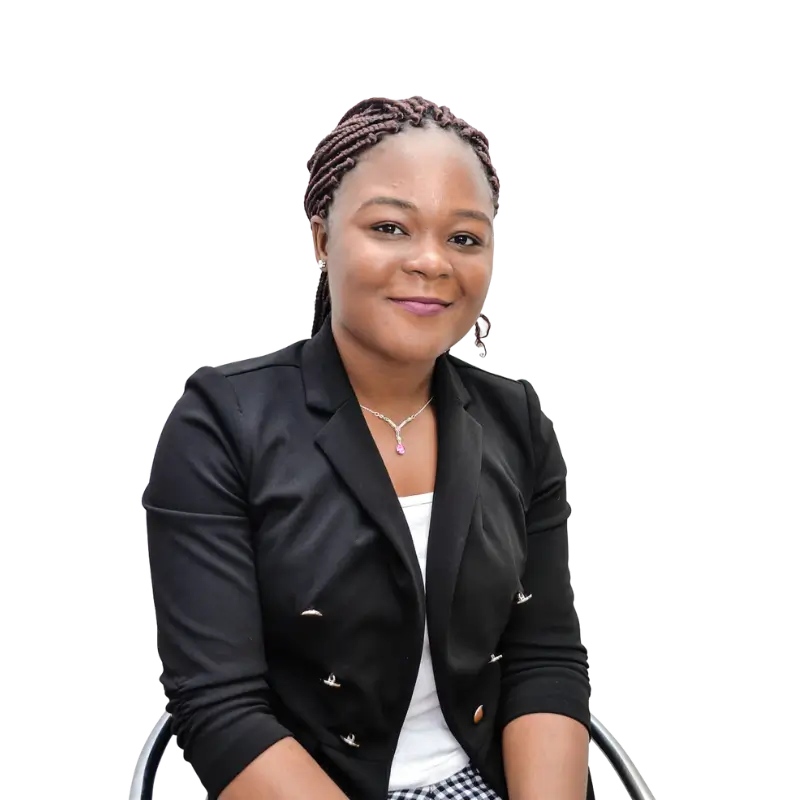 Chrissy Zimba, a black woman with long braids, wearing light pink lipstick, a white shirt with a black coat and black and white checkered pattern pants, sitting on a chair and smiling in a white background