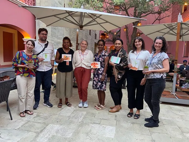 A photograph of eight people at the Human Rights Funders Network event, smiling, standing against a pink stone backdrop and holding handmade drawings.