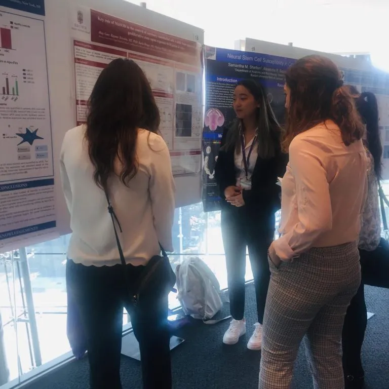 Three women gather around an academic poster at a conference.