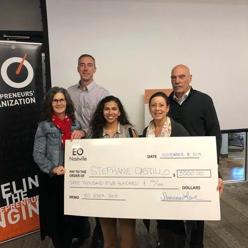 Five people pose for the camera holding a check for $5,000.