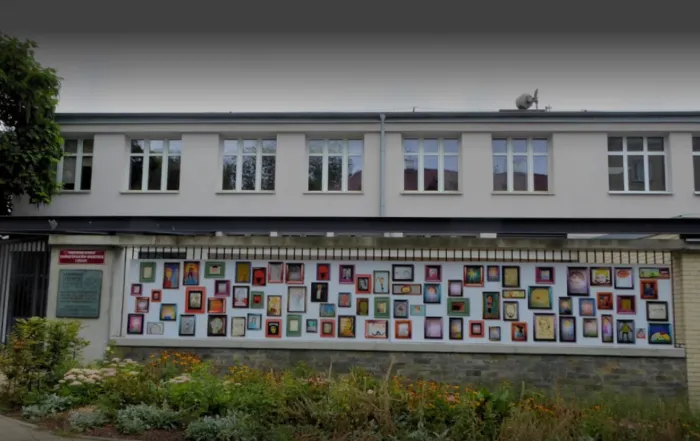 A photo of the outside of the Warsaw Centre for Socio-Educational Innovation and Training. The two-story building has a flat roof, many windows along its side second level, and is off-white colored. Along the first level are colorful works presumably made by students.