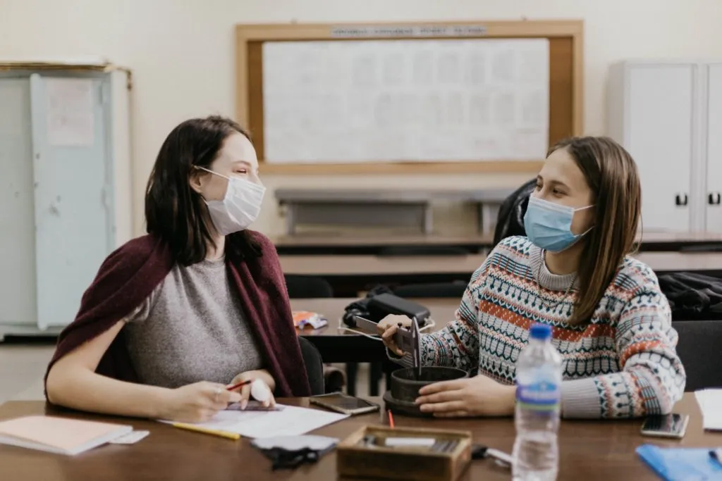 Two women wearing face masks are sitting at a lab bench and having a conversation. Around them are pieces of paper, a measuring tool, and other classroom equipment.|A colorful graphic with the text "Teaching, Difference, and Power: Insights from learning community participants."|Two refrigerator magnets that say "they" and "them" sit on top of a rainbow background.|