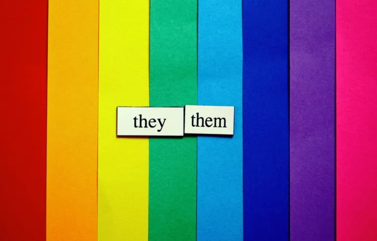 Two refrigerator magnets that say "they" and "them" sit on top of a rainbow background.
