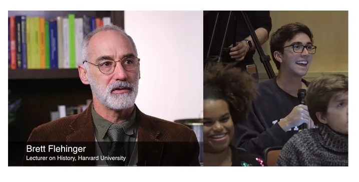 On the left, and man (Brett Flehinger, Lecturer of History at Harvard University) with glasses and short white beard faces the camera. On the right, a young man in a crowd holds a microphone and laughs.