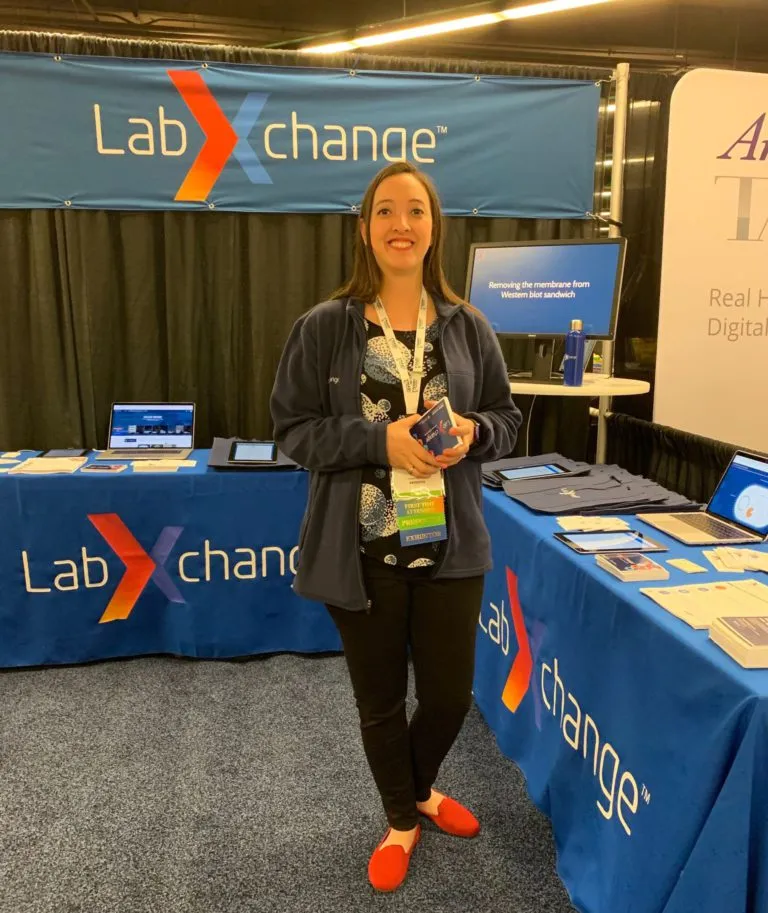 A woman poses in front of a LabXchange conference booth.