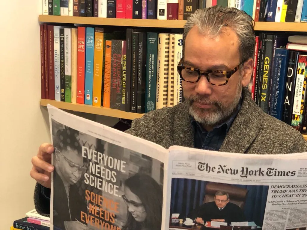 Robert Lue wearing glasses reads the New York Times newspaper