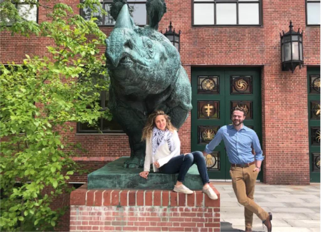 Photo of LabXchange interns Jacob Margolis and Haneen Abdo near a rhinoceros sculpture outside the Bio Labs Building.