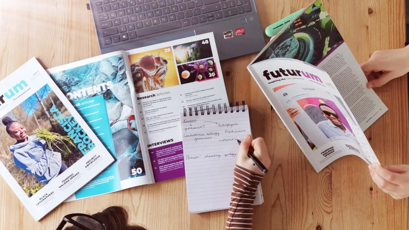 Two students read through Futurum magazines while taking notes on what they read in the articles.