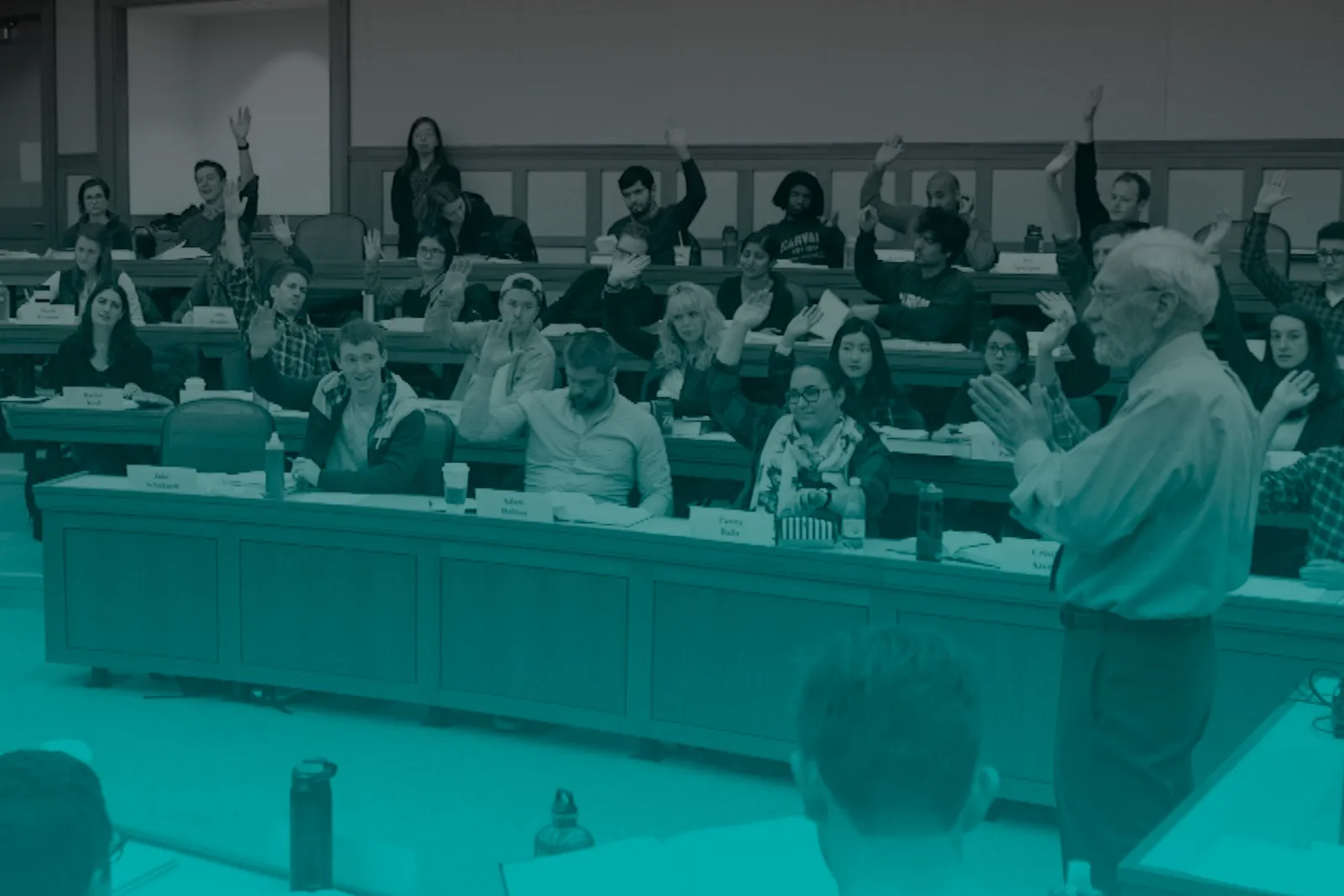 A sample classroom, with a lecturer in the foreground and rows of students in the background, many with raised hands.