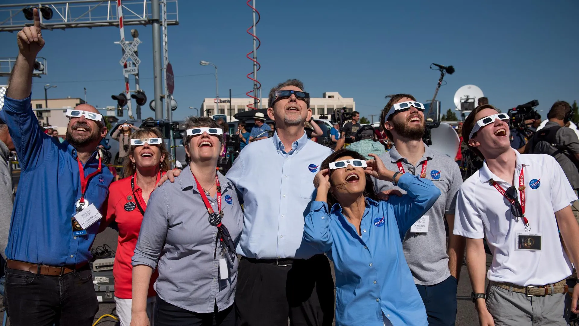 Seven NASA employees observing the 2017 total solar eclipse in Idaho Falls, Idaho. Each person is wearing eclipse-viewing glasses and smiling while looking skyward at the eclipse. 