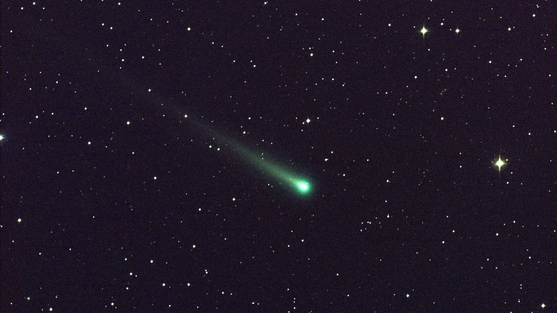 A glowing green comet streaks through the night sky, across a background of bright stars.
