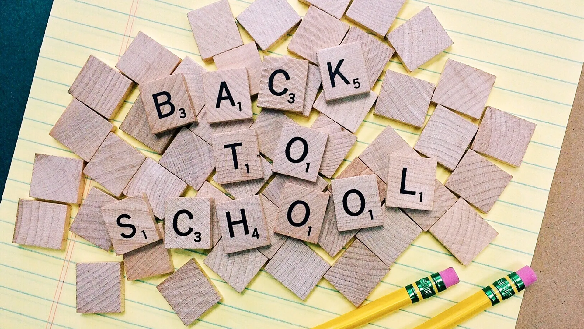 On top of a yellow paper notepad sits a pile of Scrabble tiles, face-down, with several on top of the pile face-up and arranged to spell "back to school."
