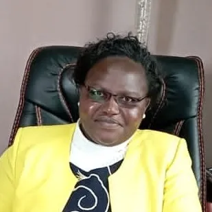 A Black woman with short black hair, wearing glasses and a bright yellow blazer.