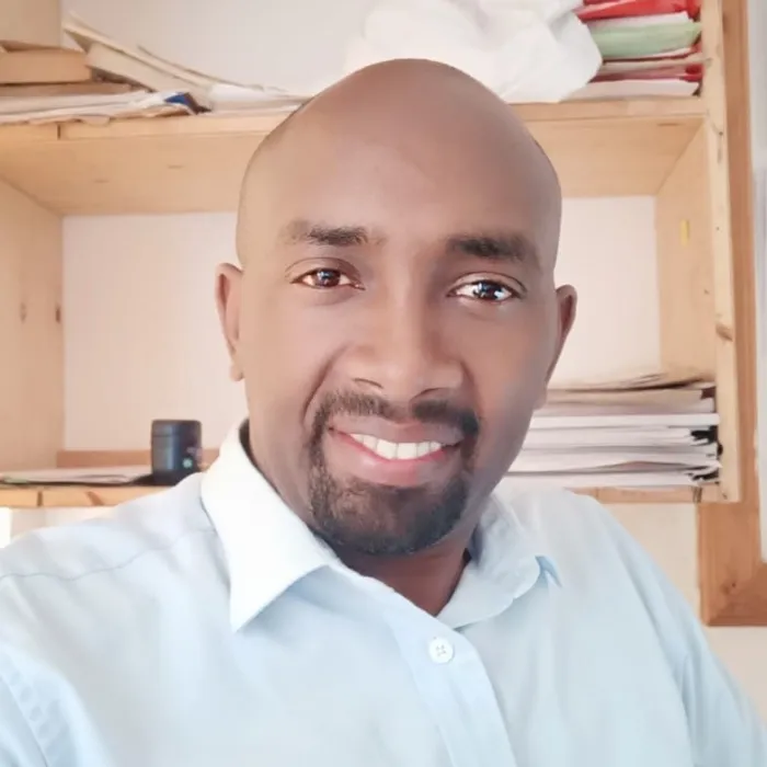 A Black man without hair except for a goatee, wearing a blue dress shirt.