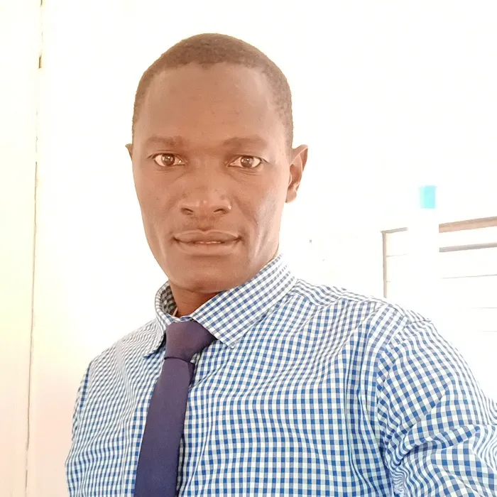 A Black man with short black hair, wearing a blue checkered dress shirt with a solid blue tie.